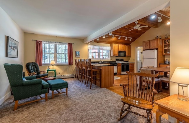 living area with ceiling fan, lofted ceiling with beams, light colored carpet, baseboard heating, and baseboards