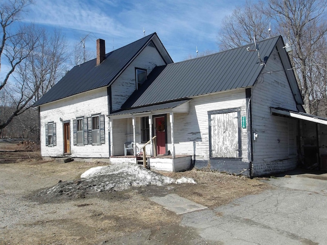 view of front facade featuring a porch, metal roof, driveway, and a chimney