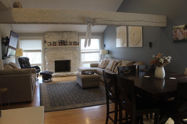 dining area featuring vaulted ceiling, wood finished floors, and a stone fireplace
