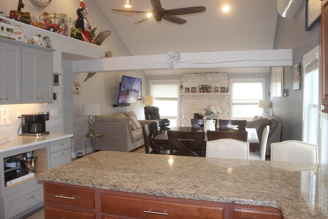 kitchen featuring light stone countertops, open floor plan, a ceiling fan, and high vaulted ceiling