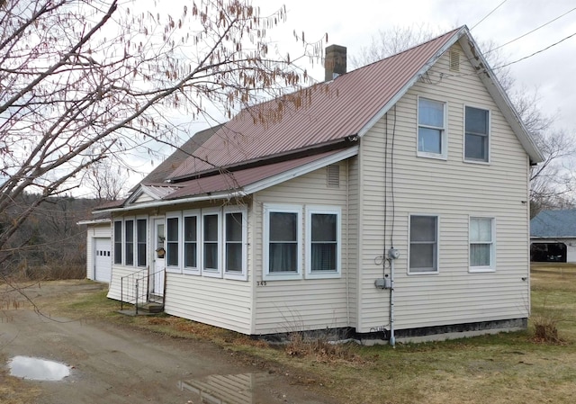 view of property exterior featuring a garage, metal roof, entry steps, and a chimney