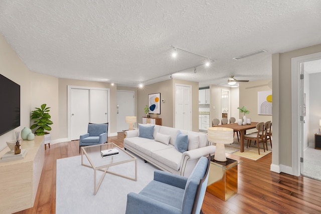living area with ceiling fan, a textured ceiling, visible vents, wood finished floors, and baseboards