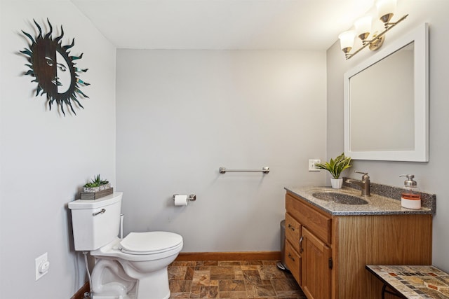 bathroom with toilet, stone finish floor, vanity, and baseboards