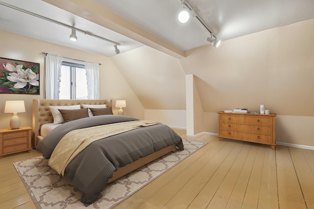 bedroom featuring rail lighting, vaulted ceiling, light wood-type flooring, and baseboards