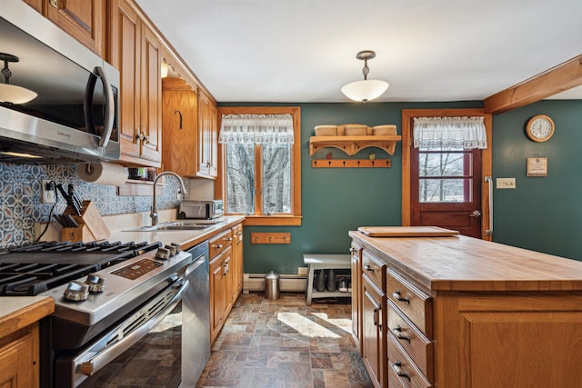 kitchen featuring a sink, wooden counters, appliances with stainless steel finishes, backsplash, and stone finish flooring