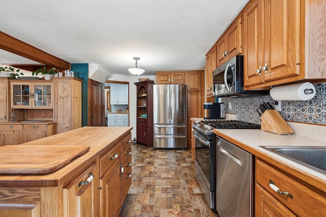 kitchen featuring butcher block counters, stone finish floor, appliances with stainless steel finishes, brown cabinets, and decorative backsplash
