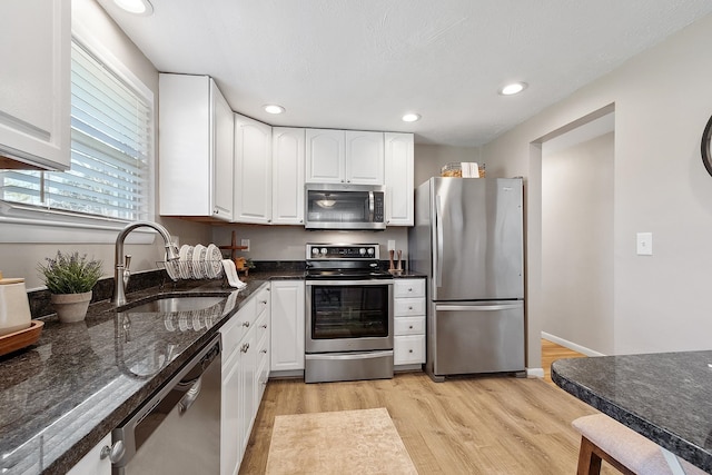 kitchen with a sink, light wood-type flooring, appliances with stainless steel finishes, and white cabinets