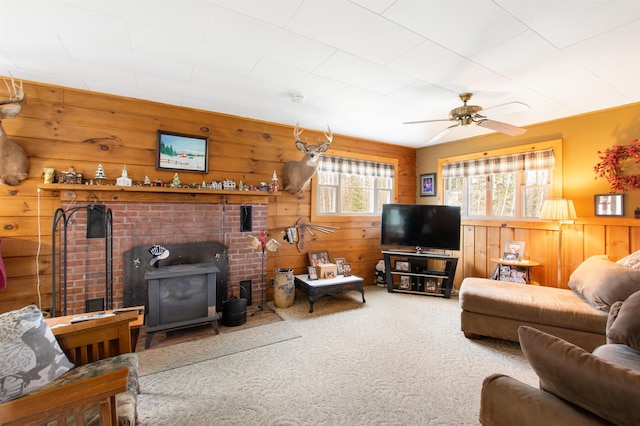 carpeted living room featuring wooden walls, a wood stove, ceiling fan, and wainscoting