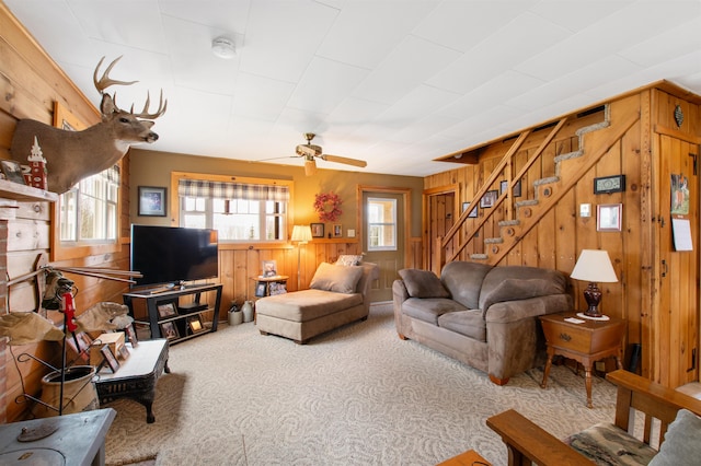 living area with wood walls, carpet flooring, plenty of natural light, and stairs