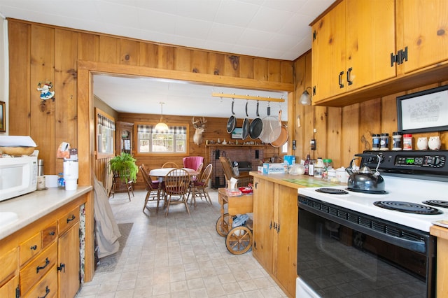 kitchen featuring wooden walls, white microwave, light countertops, range with electric stovetop, and brown cabinets