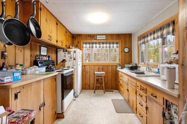 kitchen with a sink, light countertops, white appliances, wooden walls, and light floors
