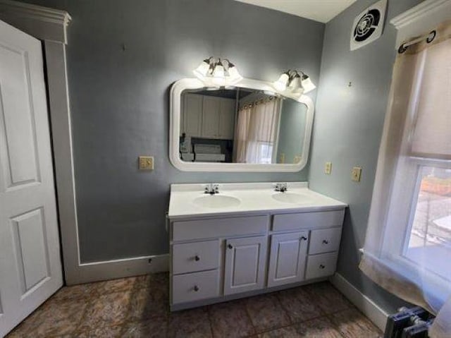 bathroom featuring a sink, baseboards, double vanity, and visible vents