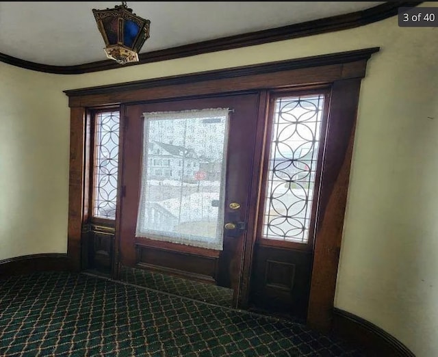 entrance foyer featuring crown molding, baseboards, and dark colored carpet