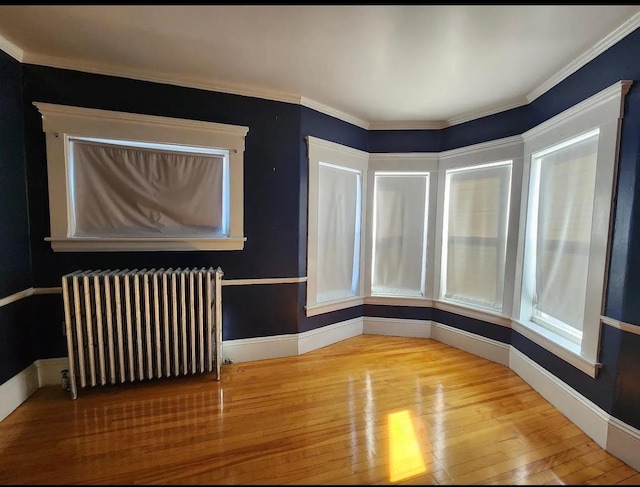 spare room featuring wood-type flooring, baseboards, ornamental molding, and radiator
