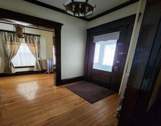 foyer entrance featuring radiator heating unit, ornamental molding, wood finished floors, and a notable chandelier