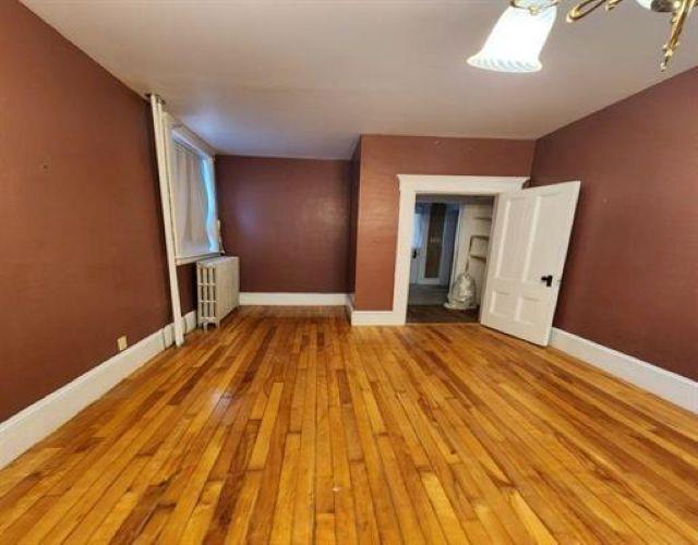 empty room featuring radiator heating unit, baseboards, hardwood / wood-style floors, and a notable chandelier