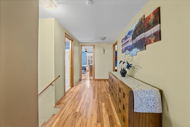 corridor with light wood-style floors, baseboards, and an upstairs landing