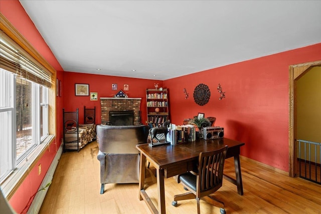dining room with baseboard heating, light wood-type flooring, and a brick fireplace