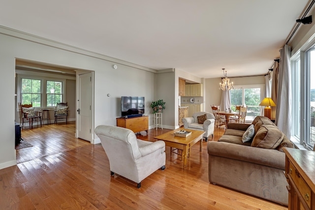 living room featuring baseboards, light wood finished floors, plenty of natural light, and an inviting chandelier