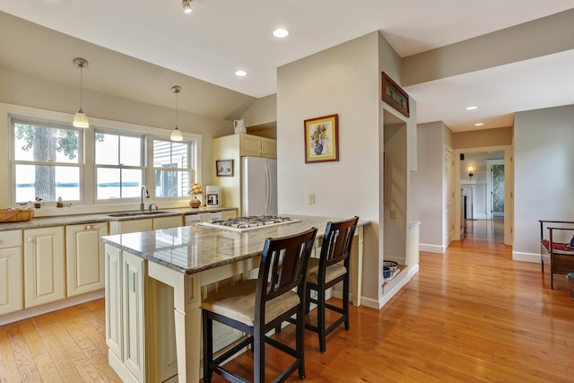 kitchen with a sink, light wood-type flooring, white appliances, cream cabinetry, and light stone countertops