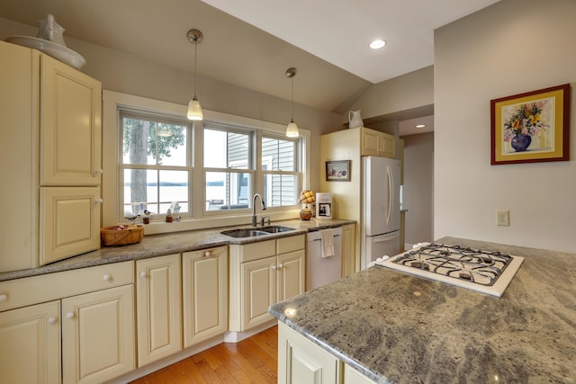 kitchen with light stone counters, white appliances, decorative light fixtures, lofted ceiling, and a sink