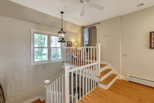 stairs with ceiling fan with notable chandelier, a baseboard radiator, wood finished floors, and baseboards