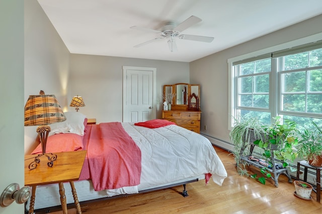 bedroom featuring a ceiling fan, a baseboard heating unit, and wood finished floors