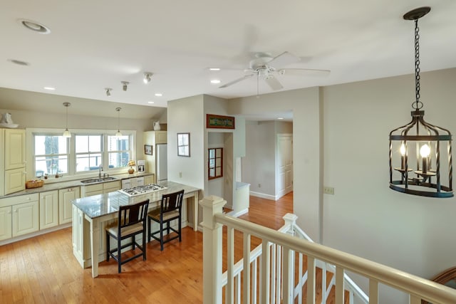 kitchen with ceiling fan, recessed lighting, light stone counters, a sink, and a breakfast bar area