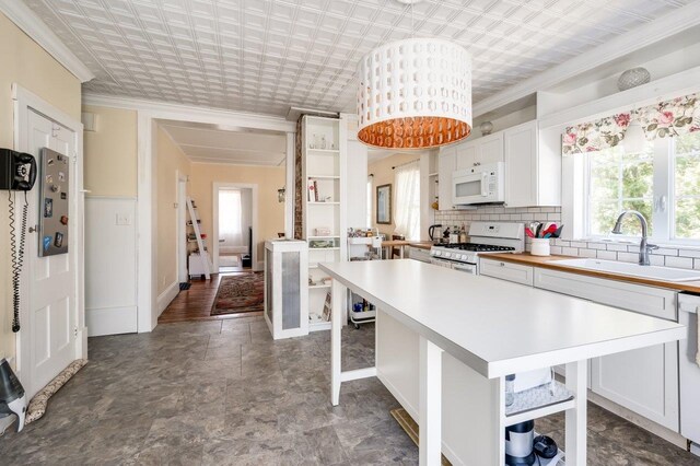 kitchen featuring ornamental molding, white appliances, light countertops, open shelves, and a sink