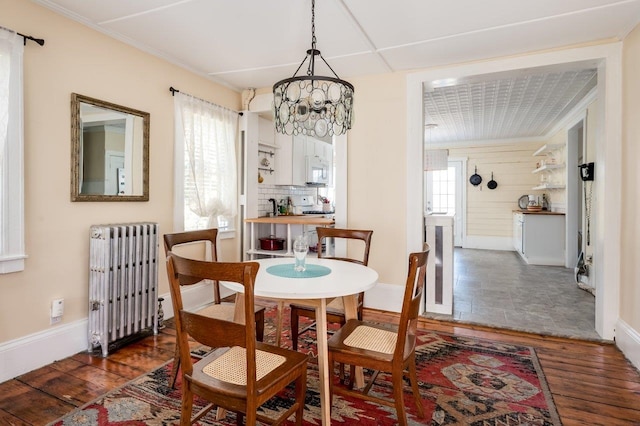 dining space with a chandelier, wood finished floors, radiator heating unit, and baseboards