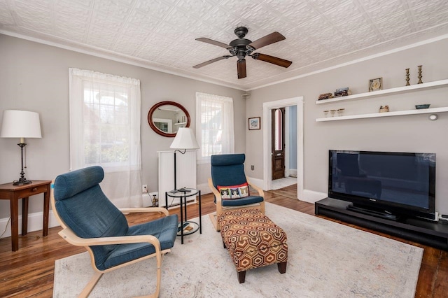 living area with wood finished floors, ceiling fan, baseboards, and ornamental molding