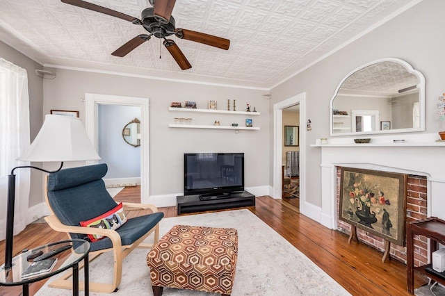 living area with baseboards, ornamental molding, an ornate ceiling, hardwood / wood-style floors, and ceiling fan