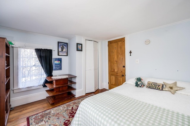 bedroom with crown molding, a closet, baseboards, and wood finished floors