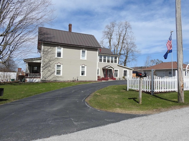 view of front of property featuring metal roof, fence, a front lawn, a chimney, and driveway