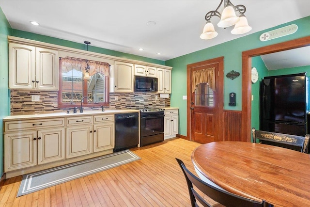 kitchen with black appliances, cream cabinetry, a sink, light countertops, and decorative light fixtures