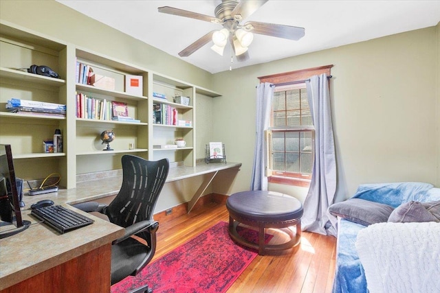 office with built in desk, built in shelves, a ceiling fan, and wood finished floors