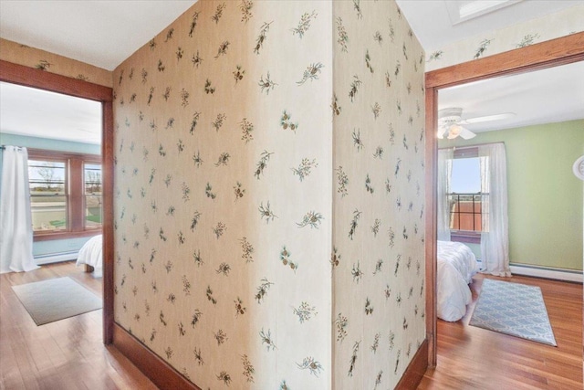 hall with wood finished floors, a baseboard heating unit, baseboards, and wallpapered walls