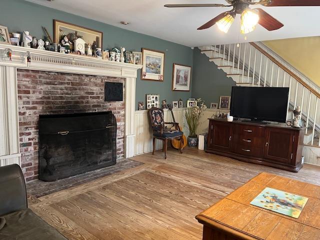 living room with light wood-style flooring, ceiling fan, a fireplace, and stairway