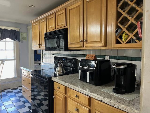 kitchen featuring tile patterned floors, light stone countertops, black appliances, and decorative backsplash