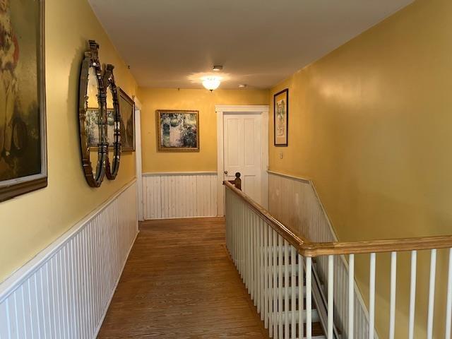 corridor with an upstairs landing, wainscoting, and wood finished floors