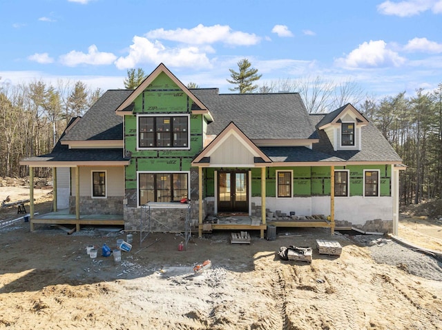 rear view of house featuring french doors, stone siding, and a shingled roof