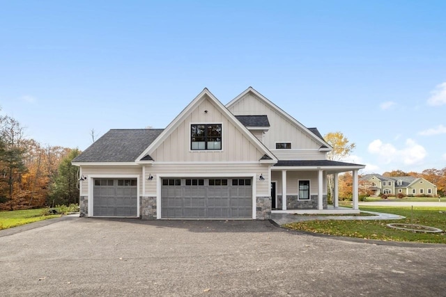 view of front of property featuring board and batten siding, a shingled roof, stone siding, and driveway