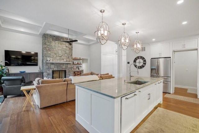 kitchen with white cabinetry, stainless steel refrigerator with ice dispenser, light stone counters, wood finished floors, and a sink