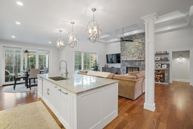 kitchen featuring recessed lighting, a fireplace, light stone countertops, a sink, and wood finished floors