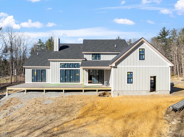 rear view of house featuring board and batten siding, a shingled roof, a wooden deck, and a chimney