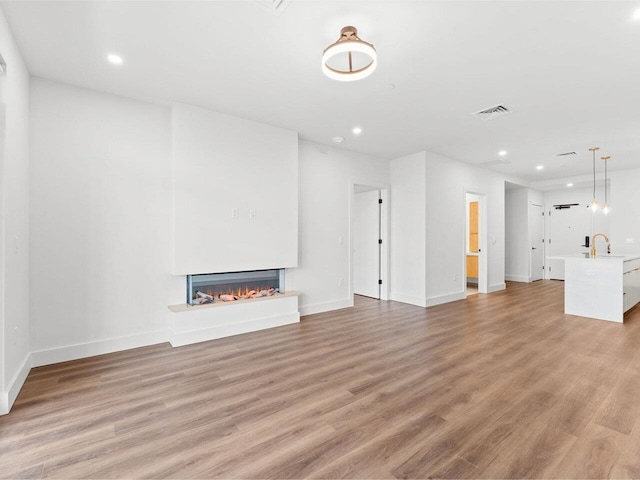 125 Cambrian Way Unit 605, Burlington, VT 05401 - unfurnished living room with a lit fireplace, recessed lighting, light wood-style floors, baseboards, and a sink