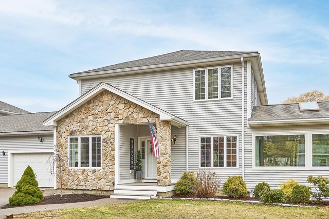 traditional-style house featuring an attached garage, roof with shingles, and stone siding