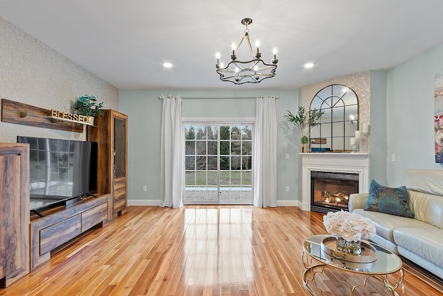 living area featuring a glass covered fireplace, light wood-style floors, baseboards, and an inviting chandelier