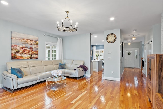 living area with light wood-type flooring, a notable chandelier, and baseboards