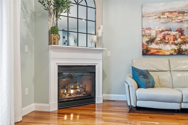 living area with wood finished floors, baseboards, a glass covered fireplace, and visible vents